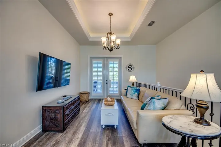 Living room featuring an inviting chandelier, dark wood-type flooring, french doors, and a tray ceiling