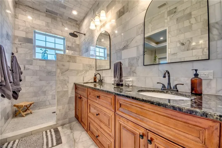 Bathroom featuring double vanity, tile walls, a tile shower, and tile patterned floors