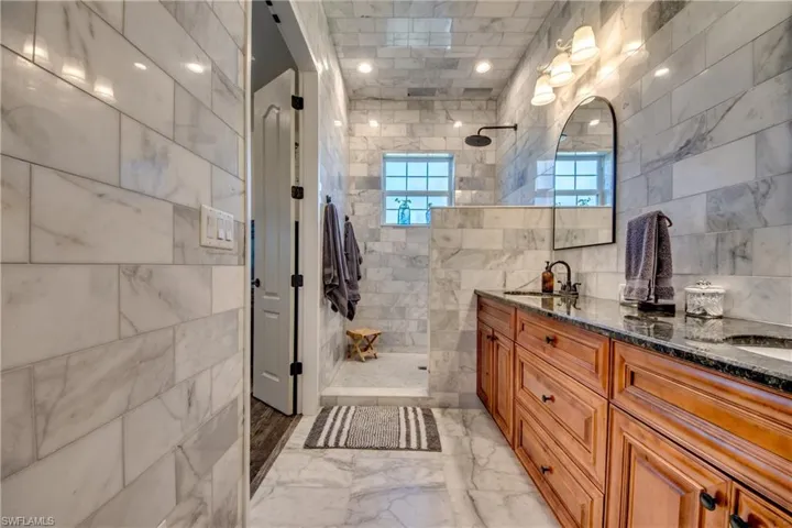 Bathroom with tiled shower, tile walls, dual vanity, and tile patterned floors