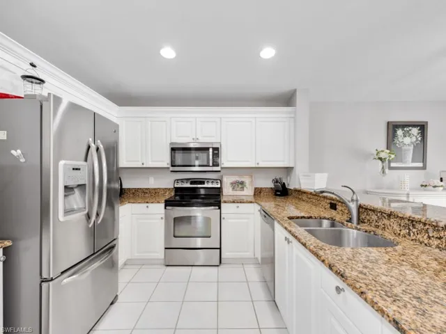 Kitchen with light stone countertops, appliances with stainless steel finishes, sink, and white cabinetry