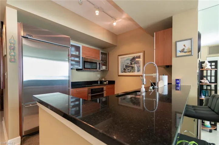 Kitchen with dark stone counters, kitchen peninsula, stainless steel appliances, rail lighting, and sink