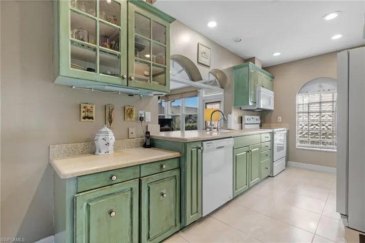 Kitchen with white appliances, green cabinets, sink, and light tile patterned floors