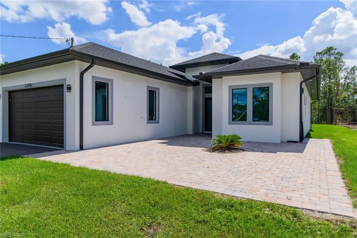 View of front facade featuring a front lawn, a garage, stucco siding, driveway, and a patio area