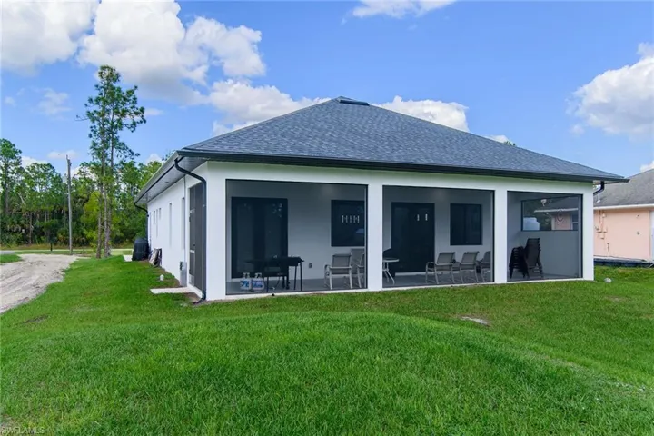 Back of house with a lawn, roof with shingles, stucco siding, and a sunroom