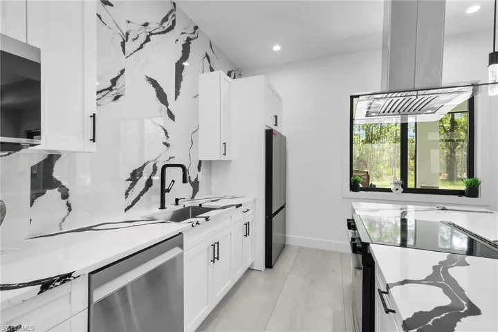 Kitchen featuring stainless steel appliances, white cabinetry, island range hood, light stone counters, and recessed lighting