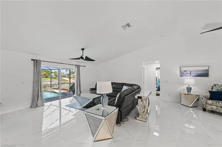 Living room featuring a ceiling fan, lofted ceiling, and light marble finish flooring
