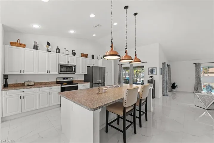 Kitchen featuring white cabinetry, a breakfast bar area, stainless steel appliances, vaulted ceiling, and light marble finish flooring