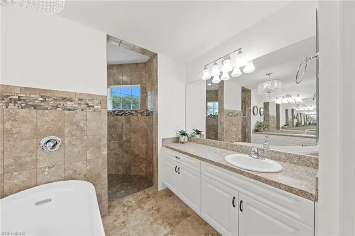 Full bath featuring suspended lighting, vanity, walk in shower, and a soaking tub