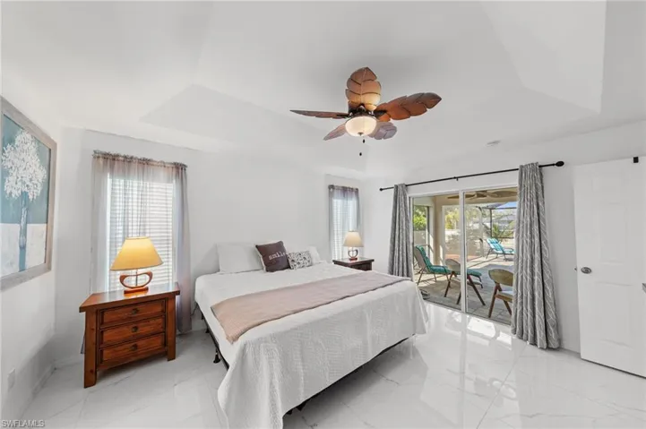 Bedroom with a raised ceiling, multiple windows, access to outside, and a ceiling fan