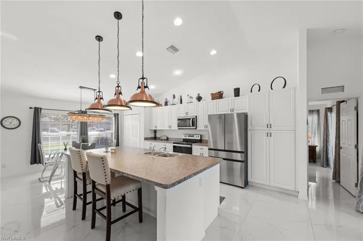 Kitchen featuring a kitchen breakfast bar, stainless steel appliances, white cabinets, vaulted ceiling, and decorative light fixtures