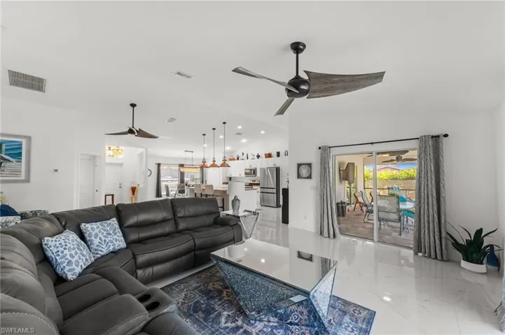 Living room featuring ceiling fan, healthy amount of natural light, lofted ceiling, and light marble finish floors