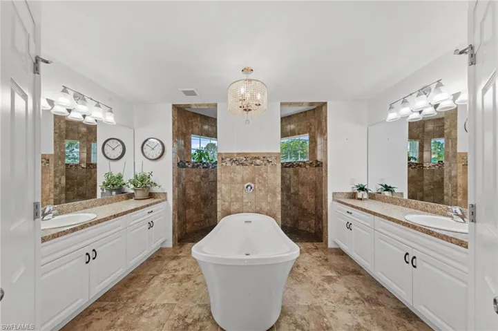 Bathroom with two vanities, a walk in shower, a freestanding bath, and hanging lights