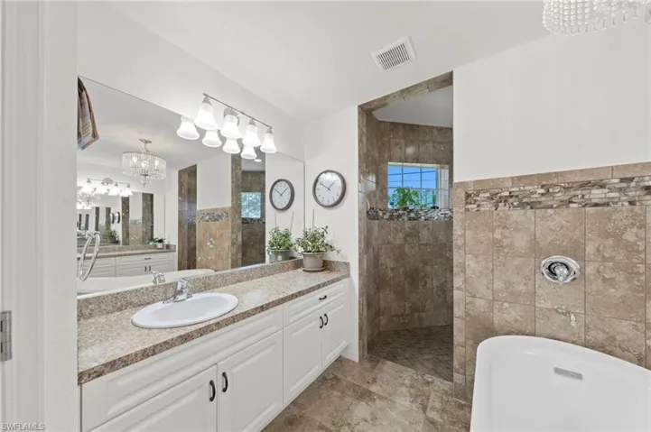 Bathroom with a chandelier, a walk in shower, vanity, and a soaking tub