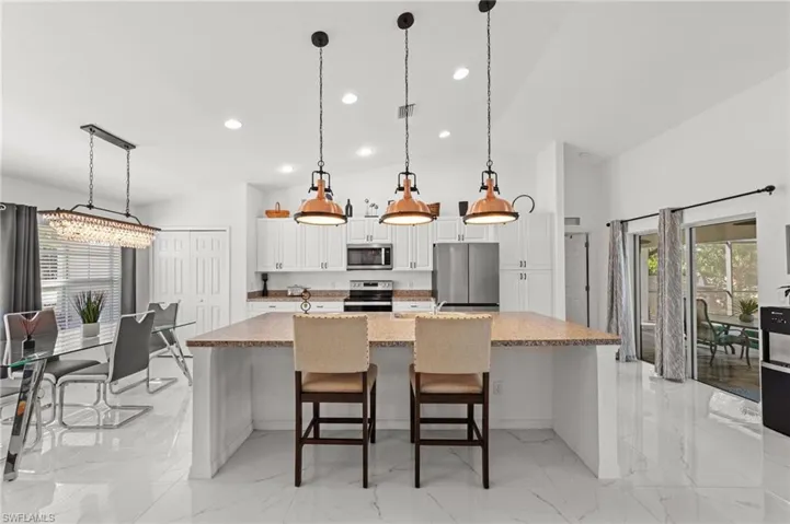 Kitchen with white cabinets, a kitchen bar, a spacious island, stainless steel appliances, and decorative light fixtures