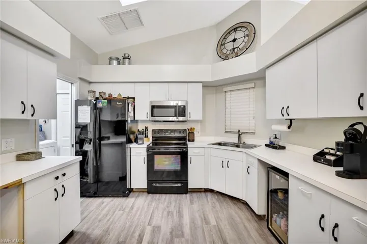 Kitchen with black appliances, light countertops, wine cooler, light wood-style flooring, and high vaulted ceiling