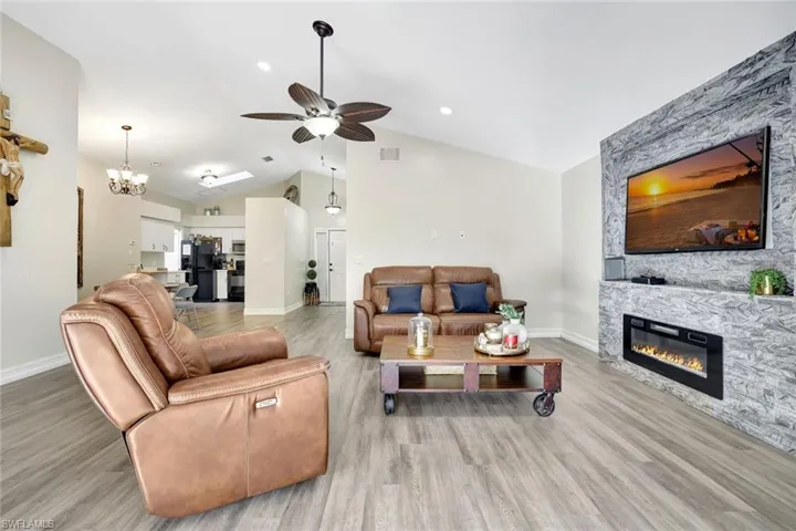 Living area with a stone fireplace, a chandelier, light wood-style flooring, a ceiling fan, and high vaulted ceiling