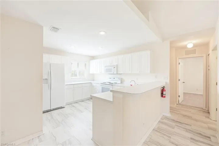 Kitchen featuring white appliances, white cabinetry, and kitchen peninsula
