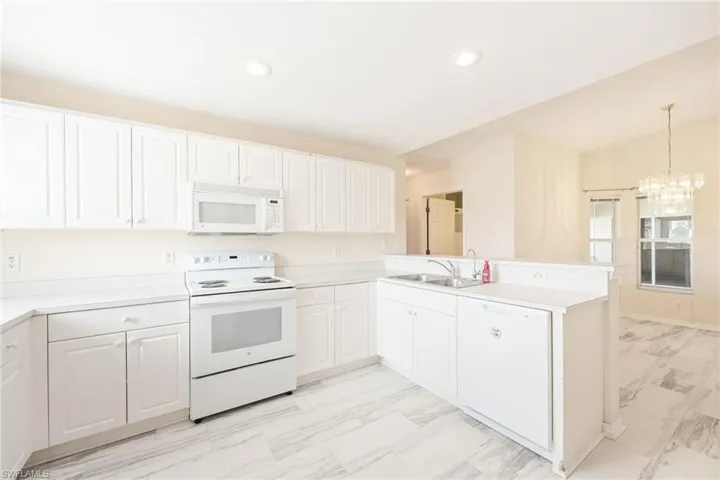 Kitchen featuring white appliances, white cabinetry, sink, and kitchen peninsula