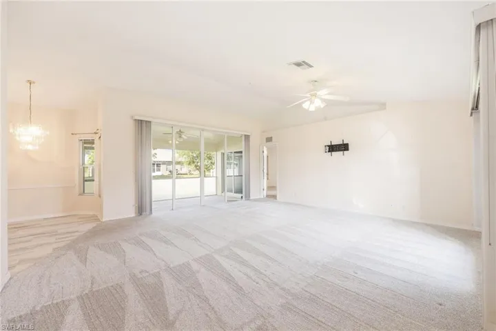 Carpeted spare room featuring ceiling fan with notable chandelier