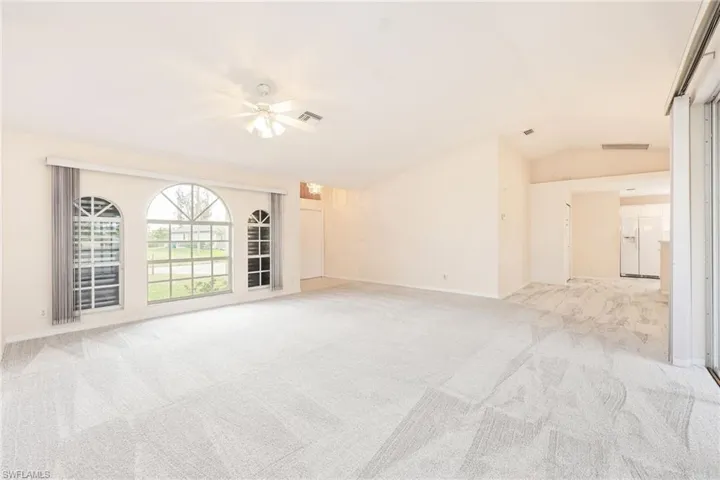 Unfurnished living room with vaulted ceiling, light colored carpet, and ceiling fan
