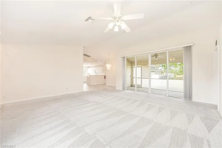 Unfurnished living room featuring light colored carpet and vaulted ceiling