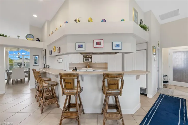 Kitchen featuring a towering ceiling, light tile patterned floors, white cabinets, a breakfast bar, and a peninsula