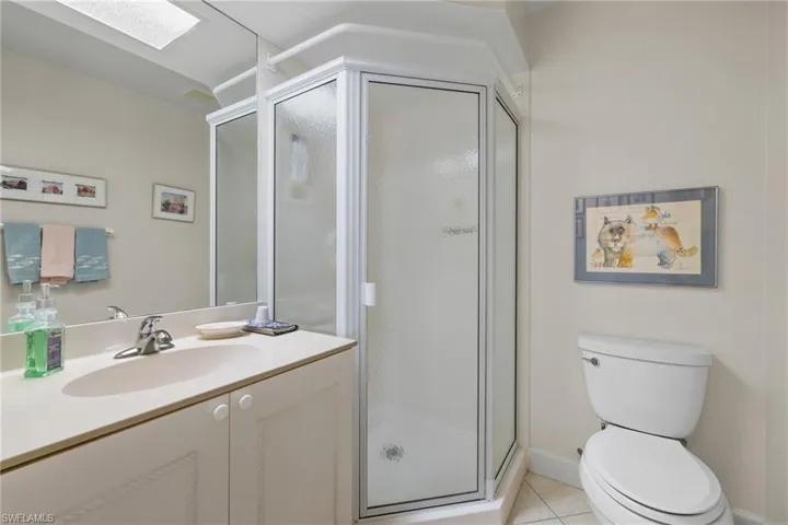 Full bathroom featuring a skylight, vanity, light tile patterned flooring, and a shower stall