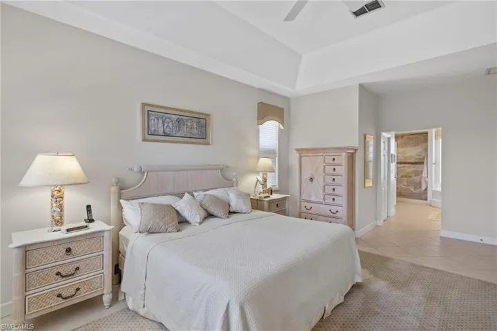 Bedroom with light tile patterned floors, ensuite bathroom, and a ceiling fan