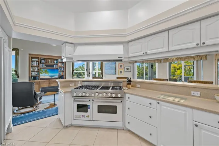 Kitchen with white cabinets, range with two ovens, light tile patterned floors, wall chimney range hood, and a towering ceiling