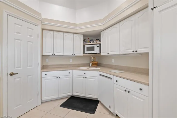 Kitchen with white cabinets, light countertops, light tile patterned flooring, and white appliances