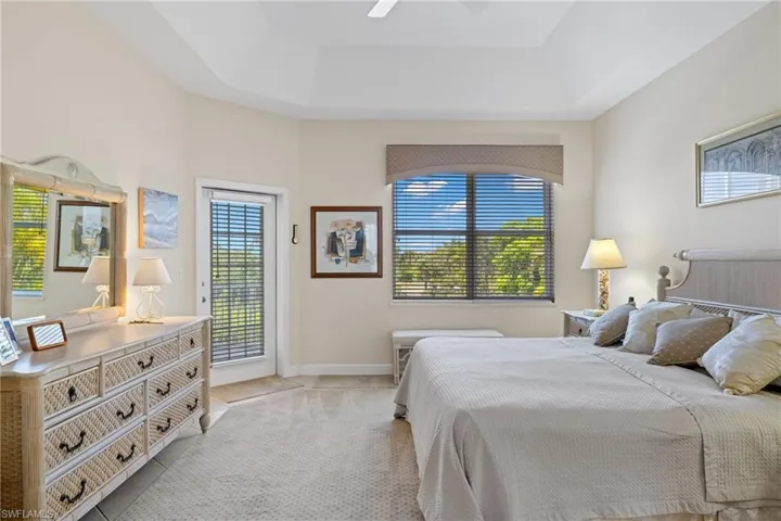 Tiled bedroom featuring multiple windows, access to outside, a tray ceiling, and a ceiling fan