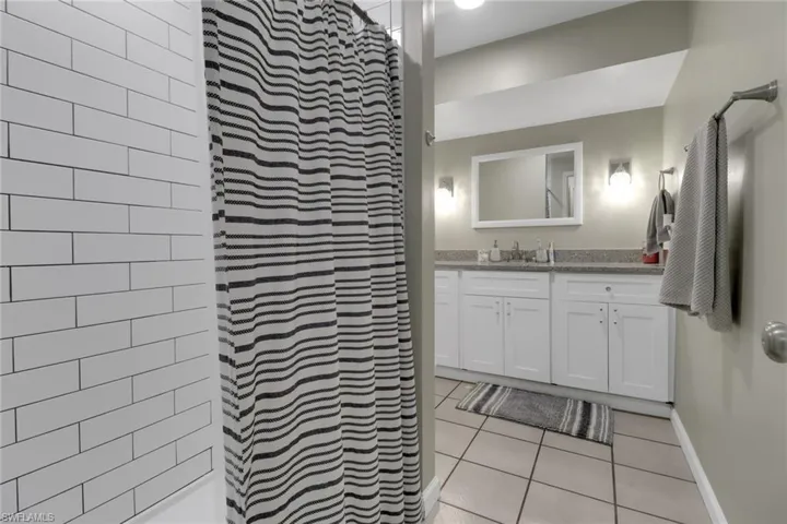 Bathroom with tiled shower, vanity, baseboards, and tile patterned flooring