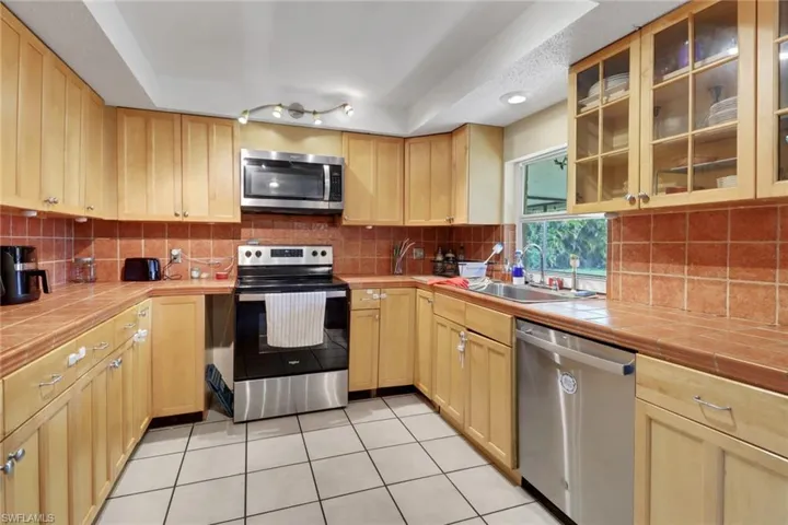 Kitchen featuring light tile patterned floors, a sink, tile counters, stainless steel appliances, and backsplash