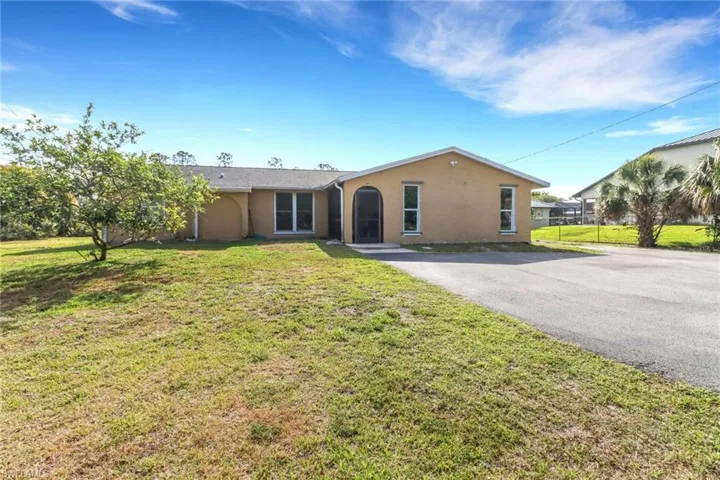 Ranch-style home featuring aphalt driveway, stucco siding, and a front lawn