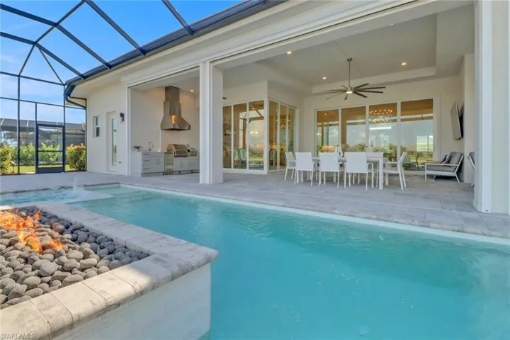 Swimming pool featuring exterior kitchen, a patio area, a ceiling fan, outdoor dining space, and a lanai