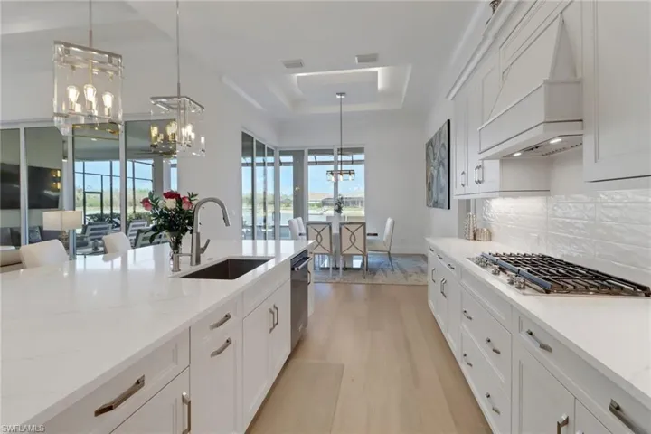 Kitchen with stainless steel appliances, a chandelier, custom range hood, light wood-type flooring, and a raised ceiling