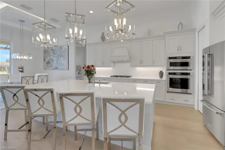 Kitchen featuring stainless steel appliances, custom range hood,  pendant chandeliers, decorative backsplash, and white cabinetry