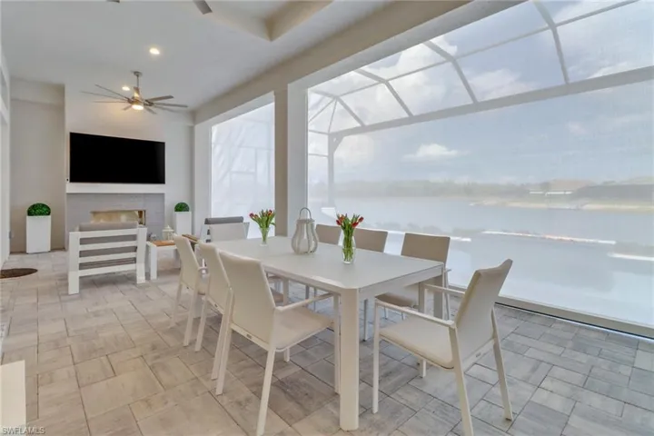 View of patio featuring a gas fireplace, ceiling fans, outdoor dining space and storm smart shutters for extra living space.
