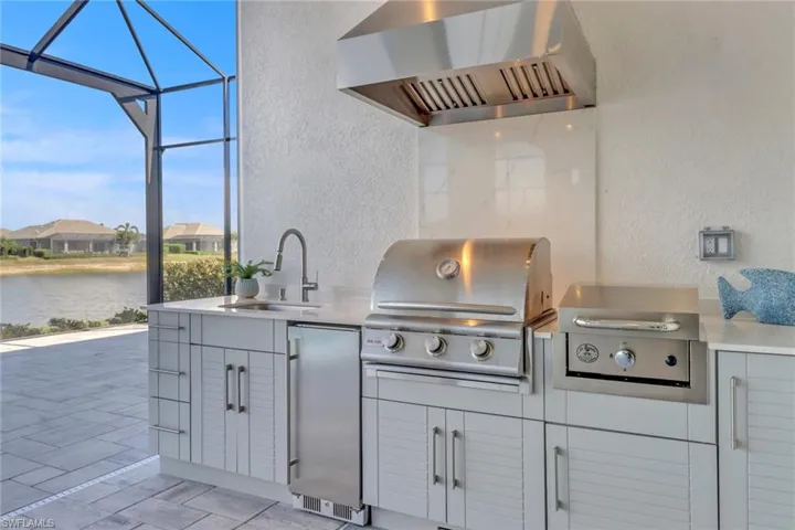 Outdoor kitchen with cabinet space, a sink, refrigerator, grill, griddle and custom stainless hood and a water view.