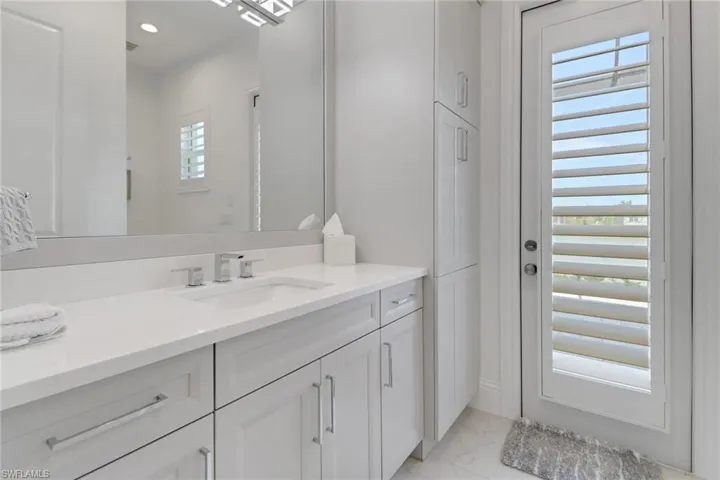 Pool bathroom with marble finish floors and vanity, door leading out to pool, also access through 3rd bedroom