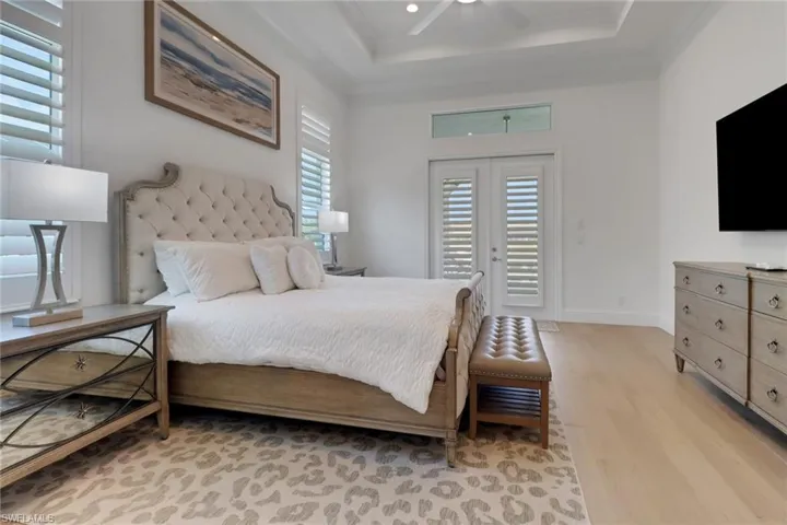 Primary Bedroom with light wood-style floors, access to exterior, a tray ceiling, and a ceiling fan