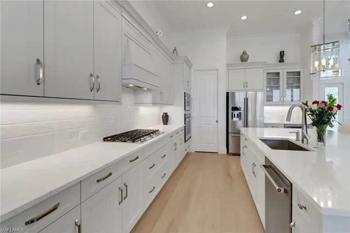 Kitchen with appliances with stainless steel finishes, gas cook top,  light wood-style floors, tasteful backsplash, ornamental molding, and pendant lighting