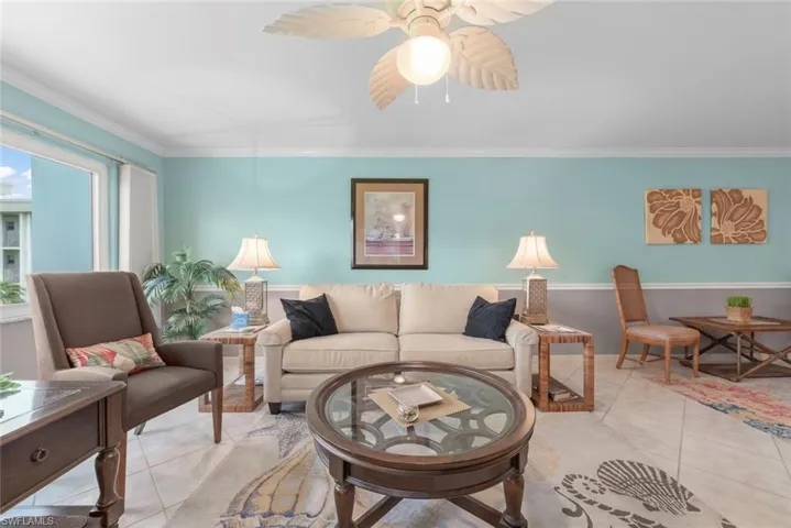 Spacious living area featuring tile flooring, a tropical-style ceiling fan, crown molding, and two-tone wall finishes