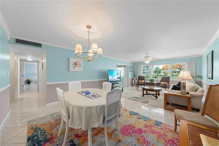 Open-concept living and dining area featuring tile flooring, crown molding, a modern gold-finish chandelier, and large windows