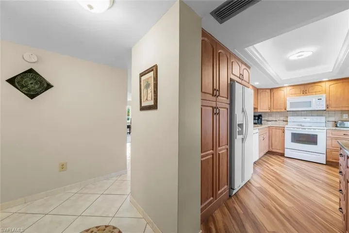 View of the kitchen featuring wood cabinetry, white appliances, and a tiled backsplash