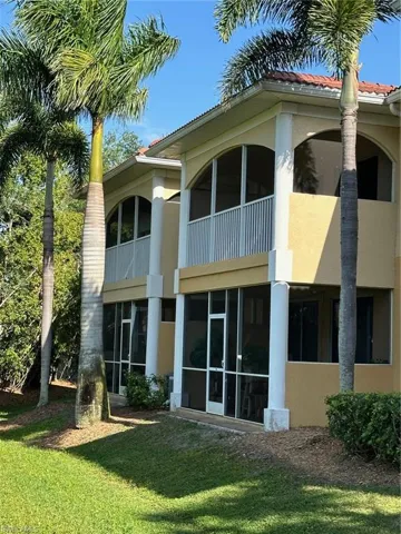 Rear view of property featuring stucco siding, a balcony, a tile roof, a sunroom, and a lawn