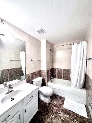 Bathroom with tile walls, vanity, shower / bathtub combination with curtain, and a textured ceiling