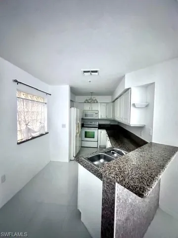 Kitchen featuring white appliances, a peninsula, white cabinets, and dark stone countertops