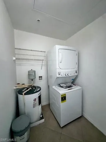 Laundry room with light tile patterned flooring, electric water heater, and stacked washer / drying machine