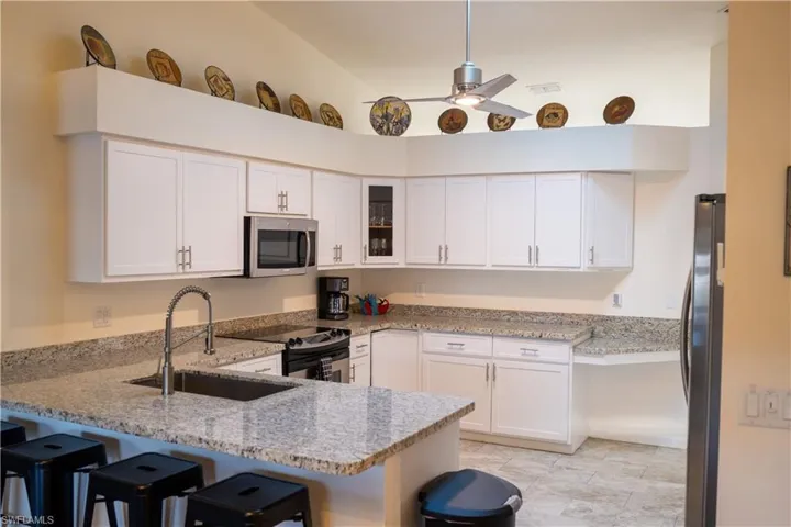Kitchen with a peninsula, white cabinetry, appliances with stainless steel finishes, light stone countertops, and glass insert cabinets